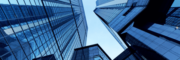 Modern glass buildings from a low-angle perspective, reflecting the sky.